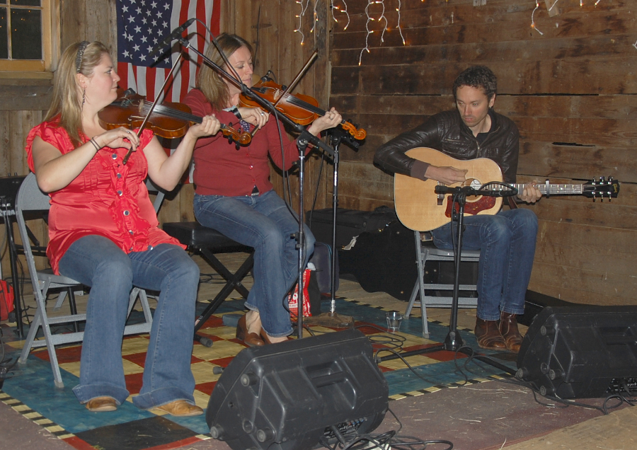 Photo of Andrea Beaton and Wendy MacIsaac on fiddles accompanied by Seph Peters on guitar